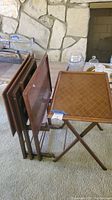 Four wooden vintage TV trays on a folding stand, shown folded together on carpeted floor.