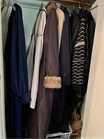 Photo showing seven women's coats and jackets hanging in a closet, including faux fur trimmed coat and beige coat.
