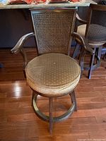 Front view showing cushioned round seat with beige fabric and small dot pattern, wooden armrests, and caned back on wooden frame.
