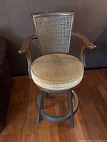 Front view of the stool showing cushioned seat, caned back, and armrests