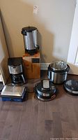 Photo shows all items: coffee urn, Instant Pot, Cuisinart coffee maker, Panini maker with 'MUE DESMOND' label, and an additional round electric appliance.