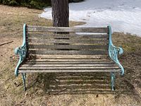 Front view of the outdoor iron and wood bench showing the weathered wooden slats and turquoise painted iron frame with decorative scrollwork.