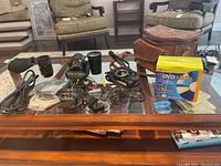 Lot contents showing four lenses, cables, chargers, camera case, and DVD discs arranged on a glass-top table.