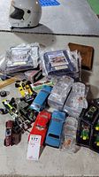 Overview of the lot showing various model cars, crystal car boxes, wall plaques, and a white racing helmet.
