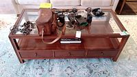 Full top view of bassett wood coffee table with beveled glass top, visible scratches, three drawers filled with various items (contents excluded from lot).