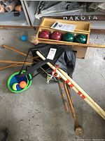 Full view of croquet and bocce ball set on concrete floor showing wooden mallets, bocce balls in box, and croquet accessories