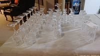 Full view of all crystal glassware arranged in rows on a white cloth, showing multiple types of stemmed glasses with clear and intricate cut glass patterns.