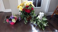 Overview of all three floral arrangements: one in red bowl, one large in basket vase, one loose bunch of white flowers