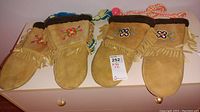 Two pairs of vintage Inuit mittens on a white surface showing tan leather, fur lined cuffs, floral embroidery, and fringed edges.