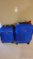 Two blue Heys luggage pieces side by side showing the size difference, wheels, handles, and fabric construction.