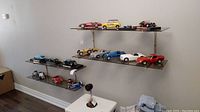 Wide shot of three glass shelves with 16 model cars in various styles and colors