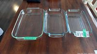 Three clear Pyrex glass baking pans placed on a wooden table, two smaller pans of same size side by side and a larger pan.