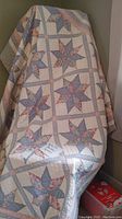 Full view of quilt draped over a chair, showing the overall pattern and color scheme with star-shaped patchwork blocks and pastel borders.