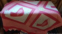 Full view of handmade vintage quilt covering bed, showing pink bird blocks with white backgrounds and pink borders framing each block.