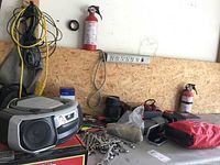 Wide view showing assorted hand tools (wrenches, screwdrivers) on a workbench, radio/CD player, power inverter, extension cords, and fire extinguisher mounted on plywood board.