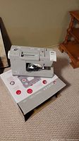 Sewing machine sitting on its original box with power cord and foot pedal bag visible