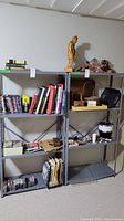 Three metal shelving units together in a basement setting, partially filled with books, baskets, a wooden statue, and other household items (not included).