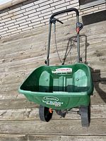 Full front view of green Scotts Turf Builder Edguard DLX fertilizer spreader showing plastic hopper, metal handle with control lever and wheels