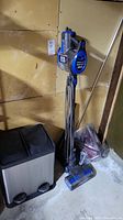 Shark upright vacuum cleaner standing against a wall with cord wrapped.