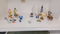 Full group of assorted hand-painted ceramic figurines including birds, animals, houses, and human figures displayed on a white shelf.