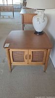 Front view of the mahogany side table showing the square top, caned doors, and tapered legs.