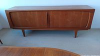 Front view of teak sideboard with sliding doors closed, showing overall shape and leg design