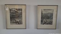 Two vintage black and white photographs framed and hanging on a wall, showing mountainous landscapes with one image including a person and horse.