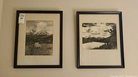 Two framed black and white photographs hung on a wall, showing mountain and lake landscapes.