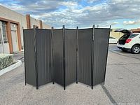 Front view of 6 panel black fabric room divider standing outdoors, showing all panels fully extended.
