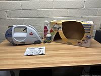Full view of Bissell Spot Lifter Power Brush handheld carpet cleaner, user guide, cleaning solution, and original box on wood table.