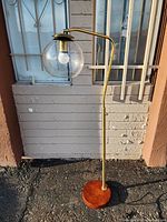 Full view of the floor lamp showing the round wooden base, brass/gold toned pole and arm, and the clear glass globe shade with exposed bulb.