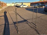 Full view of black metal garment rack standing on pavement showing hanging bar and base shelf.
