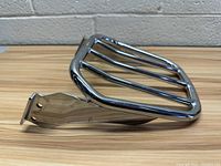 Chrome Harley Davidson custom tapered sport luggage rack shown on wooden table from side angle, showing mounting brackets and three horizontal bars.