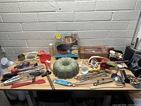 Wide view of the entire assortment of vintage kitchen tools and bakeware on two tables against a brick wall.