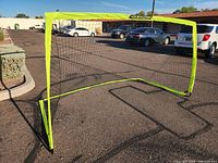 Soccer goal viewed diagonally from the side, showing yellow frame and attached black net, placed on asphalt.