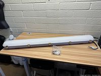 Full view of the LED waterproof shop light laid on desk showing mounting clips and wiring end.