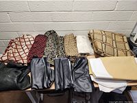 Lot of assorted fabrics showing colorful printed textiles, black leather pieces, and plain beige and white fabrics arranged on a table