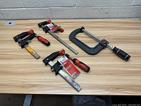 Four clamps on wood table showing Bessy and Husky brands and different clamp styles and sizes.
