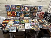 Wide-angle photo showing 36 DVDs arranged on a table against a beige brick wall, showing a diverse set of movies and genres.