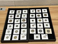 Two trays showing 34 foreign coins mounted in holders with labels of country, year, and denomination