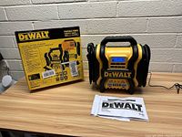DeWalt portable battery charger and jump starter placed on wooden surface with original box and manual next to it.