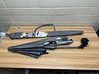 Photo of folded gray Versa Brella umbrella with black metal clamp mount and gray carrying case on wooden table.