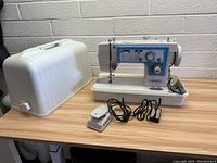 Front and left side view of the vintage Dressmaker sewing machine with carrying case and foot pedals on a wooden table.