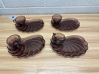 Four vintage purple glass bistro sets displayed on a light wood table, each set consisting of one cup and one shell-shaped plate.