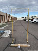 Full view of the gold metal arch backdrop standing upright outdoors on paved area with buildings and cars in background.