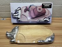 Photo of pig shaped cutting board showing the wooden body with metal pig head and tail accents in front of box packaging.
