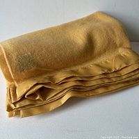 Folded mustard yellow wool blanket with satin edge binding on a table