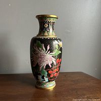 Full front view of the cloisonne vase showing floral and bird enamel designs over a black gold background on a wooden surface.