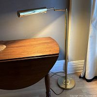 Full view of vintage brass swing arm floor lamp positioned next to wooden furniture showing the lamp's height and swing arm extension.