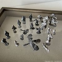 Top view of 25 pewter fantasy miniatures on a flat surface, showing characters including a flying dragon, hooded figures, and warriors.